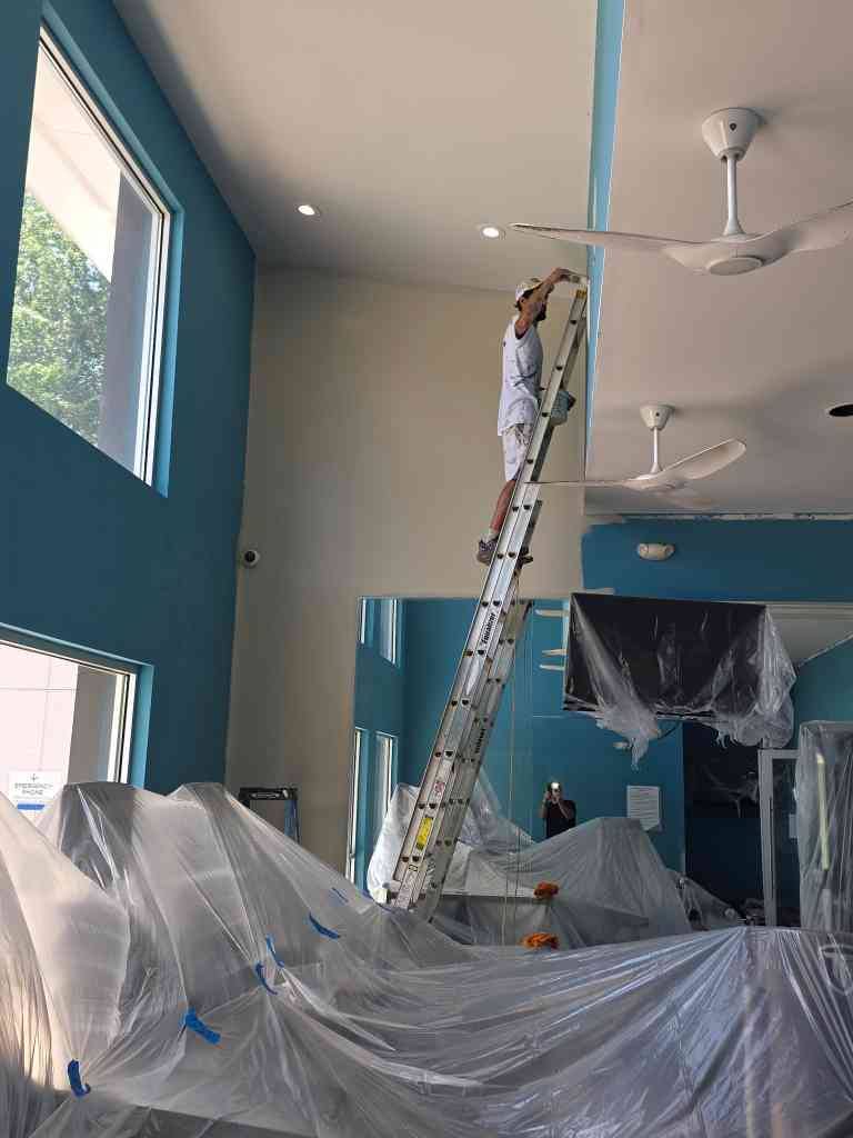 David painting a two-story commercial wall from an extension ladder